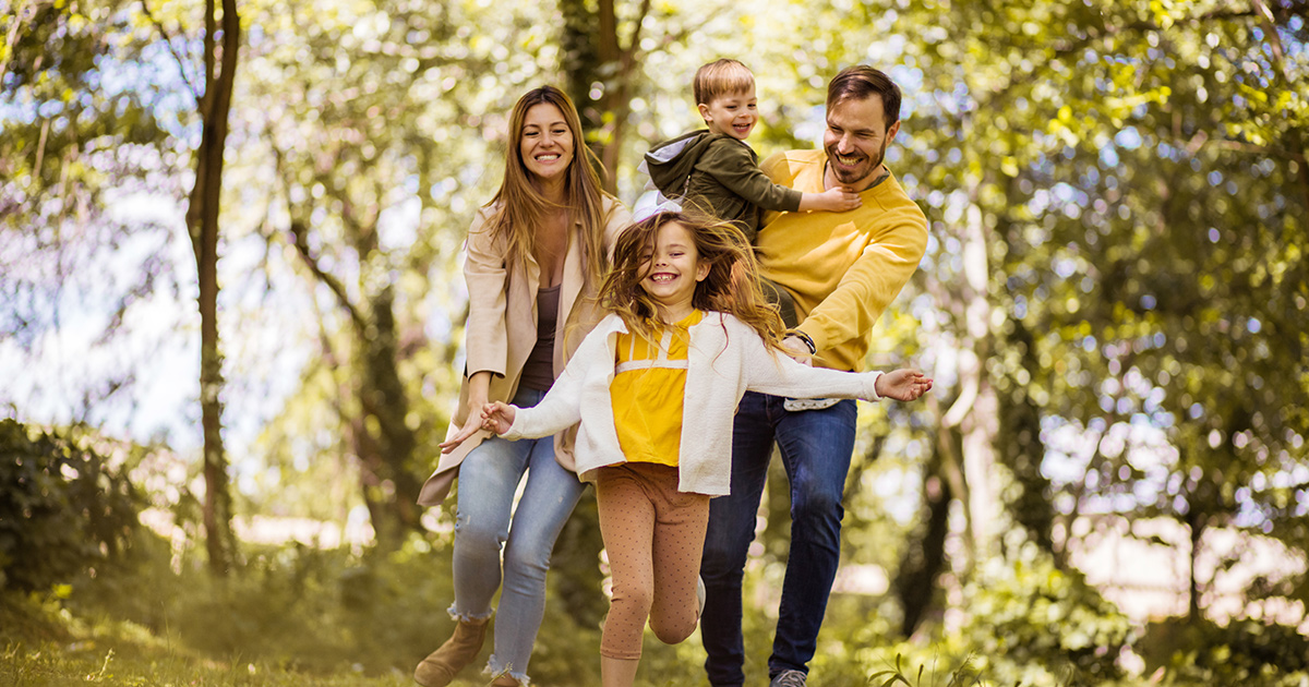 Family of four smiling and posing for a photo together outside.