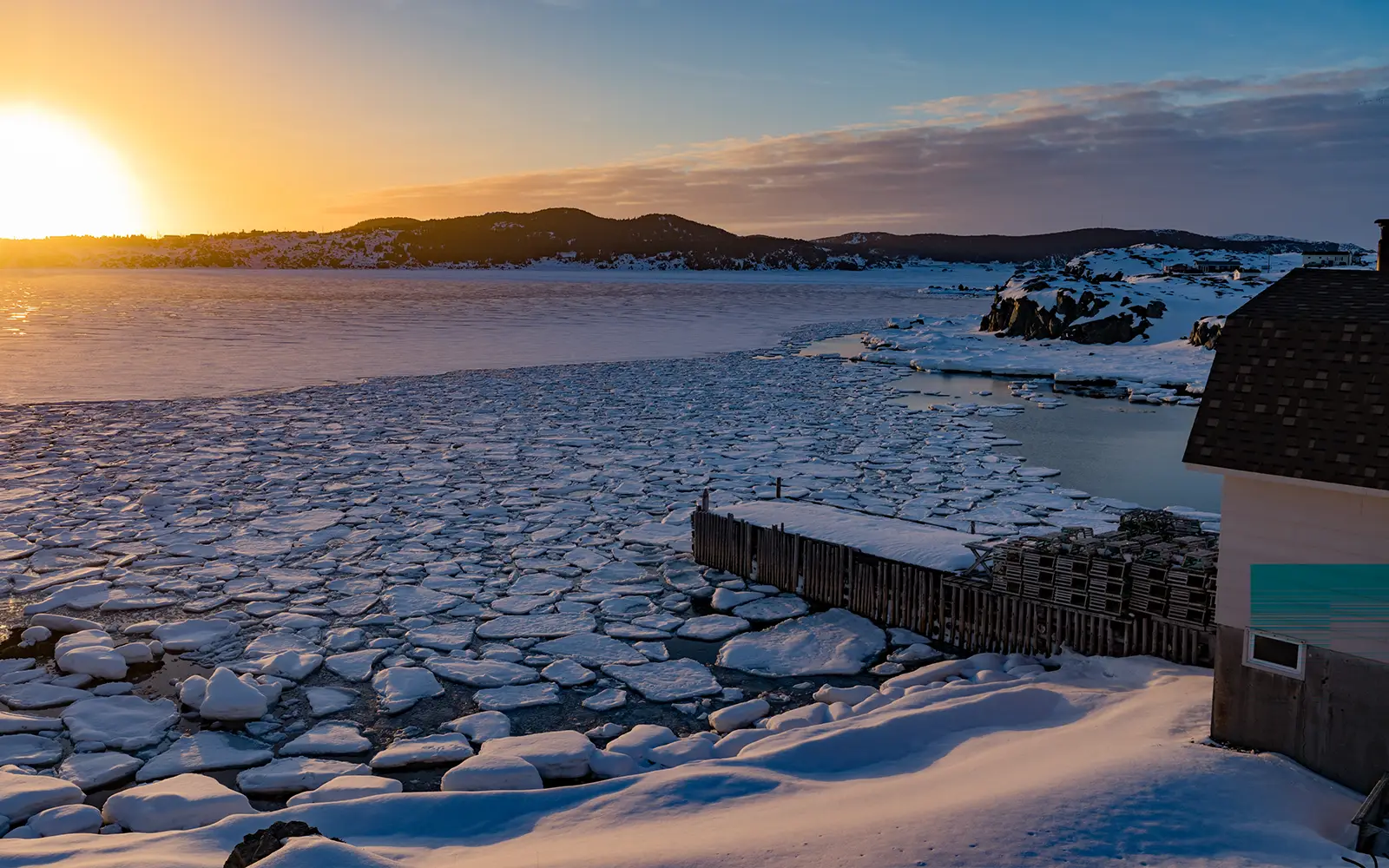 Winter scene of cracked ice on the edge of a river with hills off in the distance with a sunrise