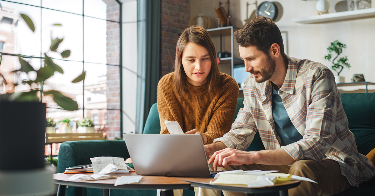 Couple using laptop on apartment couch checking bills