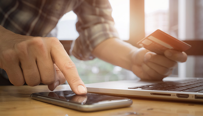 Person in front of a laptop on their cellphone holding a credit card