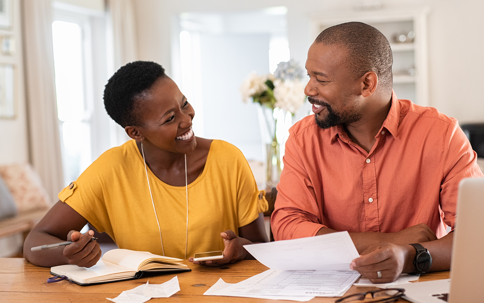 Couple sitting at table smiling while looking at papers on the table.