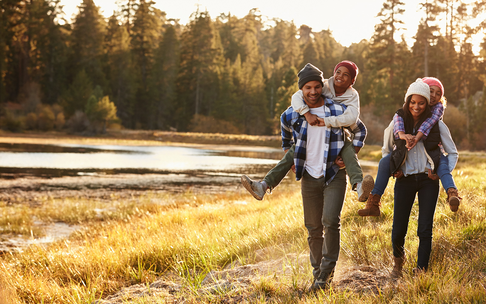 Parents Giving Children Piggyback Ride On Walk By Lake