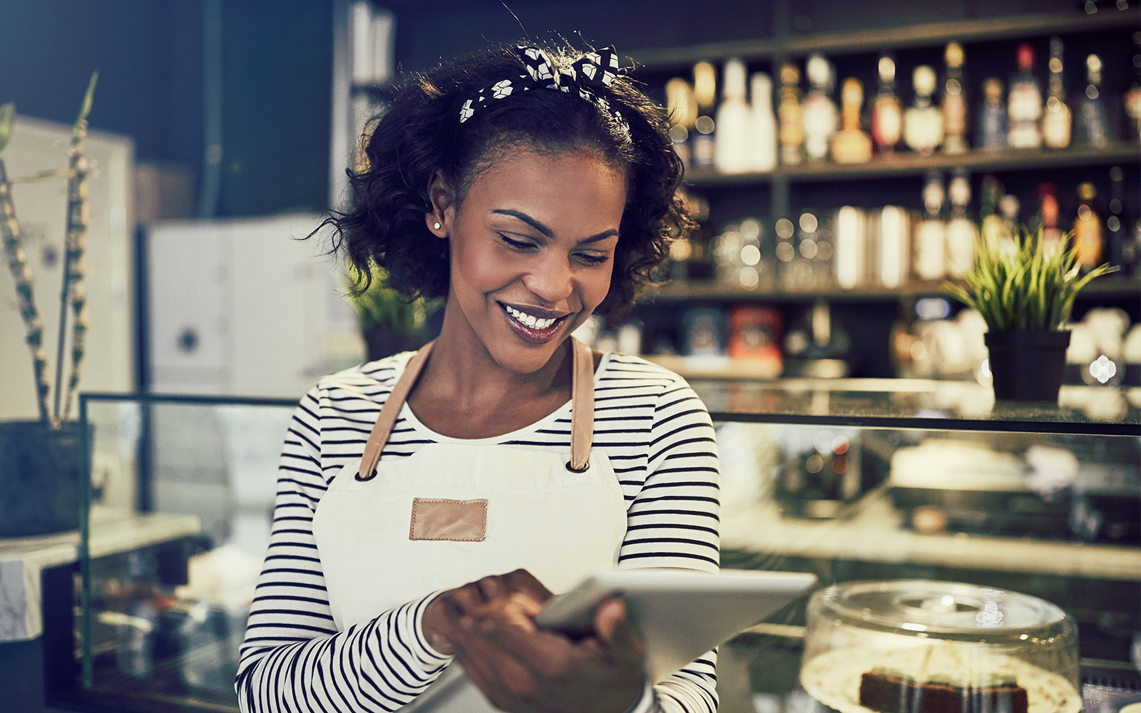 Entrepreneur working with a digital tablet while standing in front of the counter of her trendy cafe