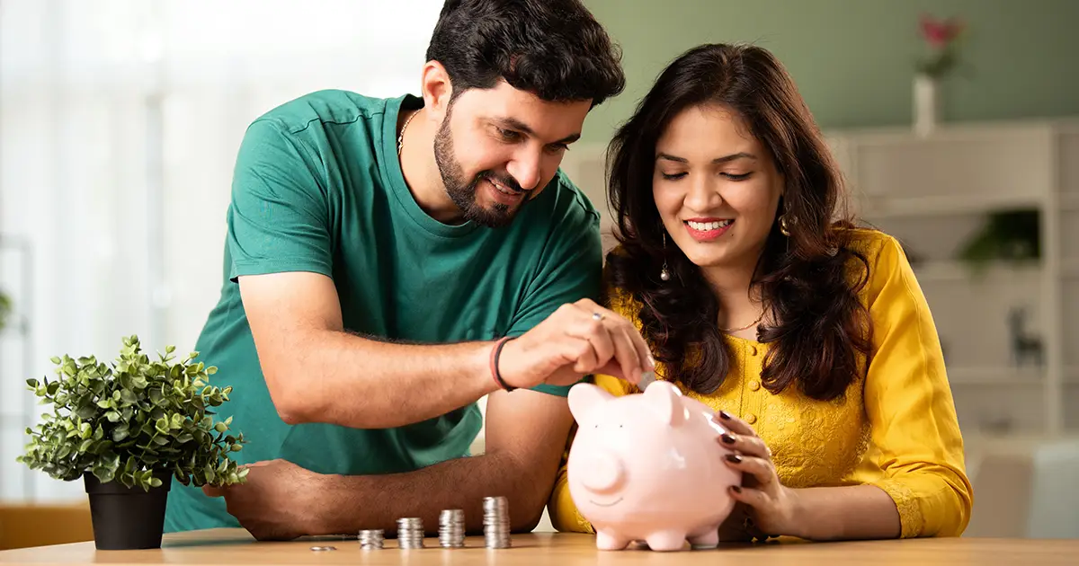 A couple showing the saving concept of putting coins in a piggy bank.