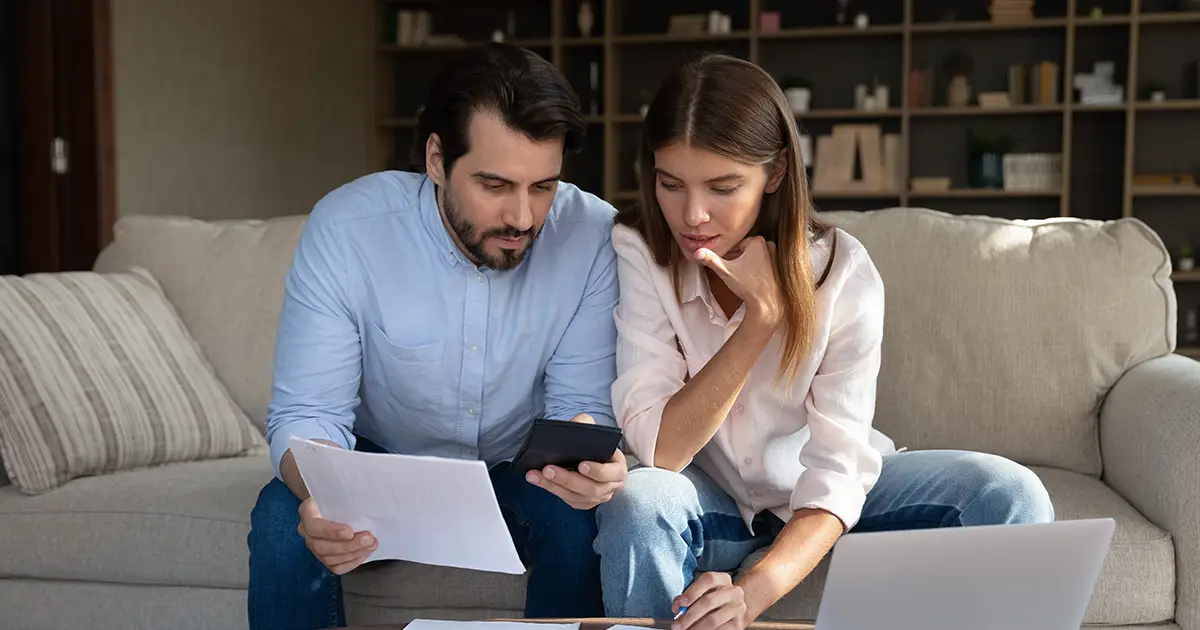 Focused husband and wife sit at table at home looking at paperwork.