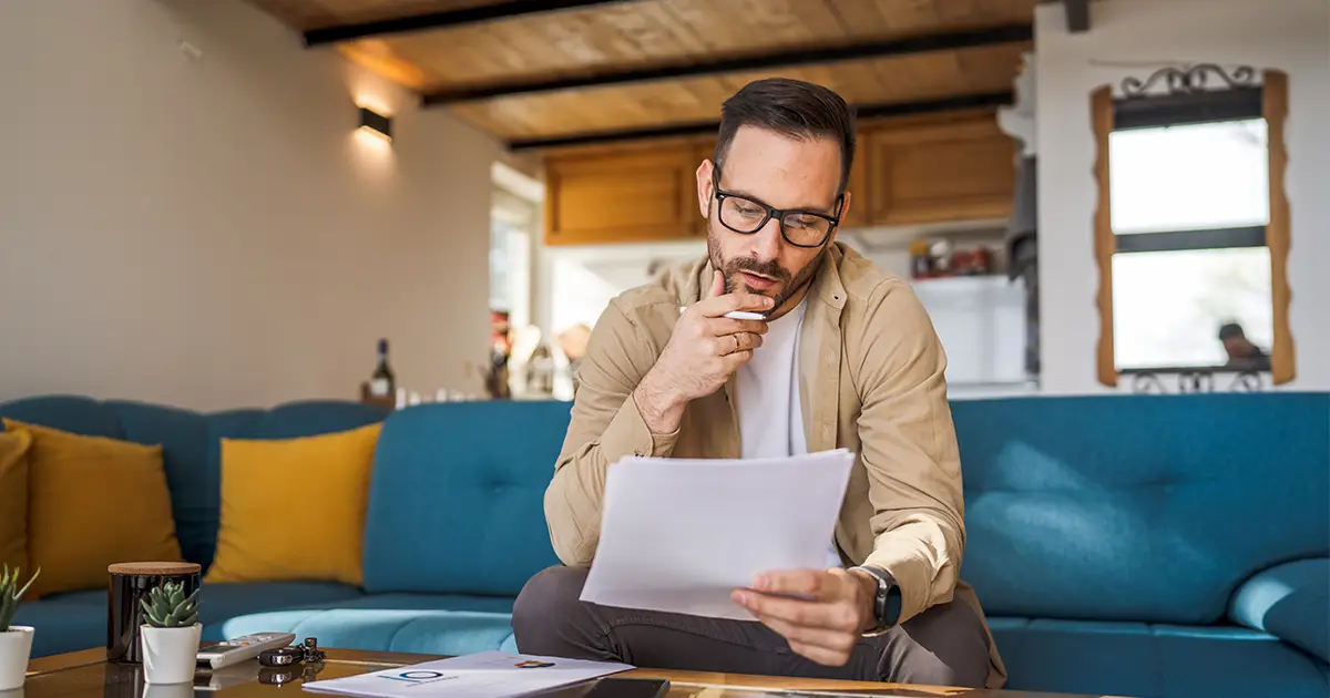 A man sitting on the couch working at home holding paper documents.