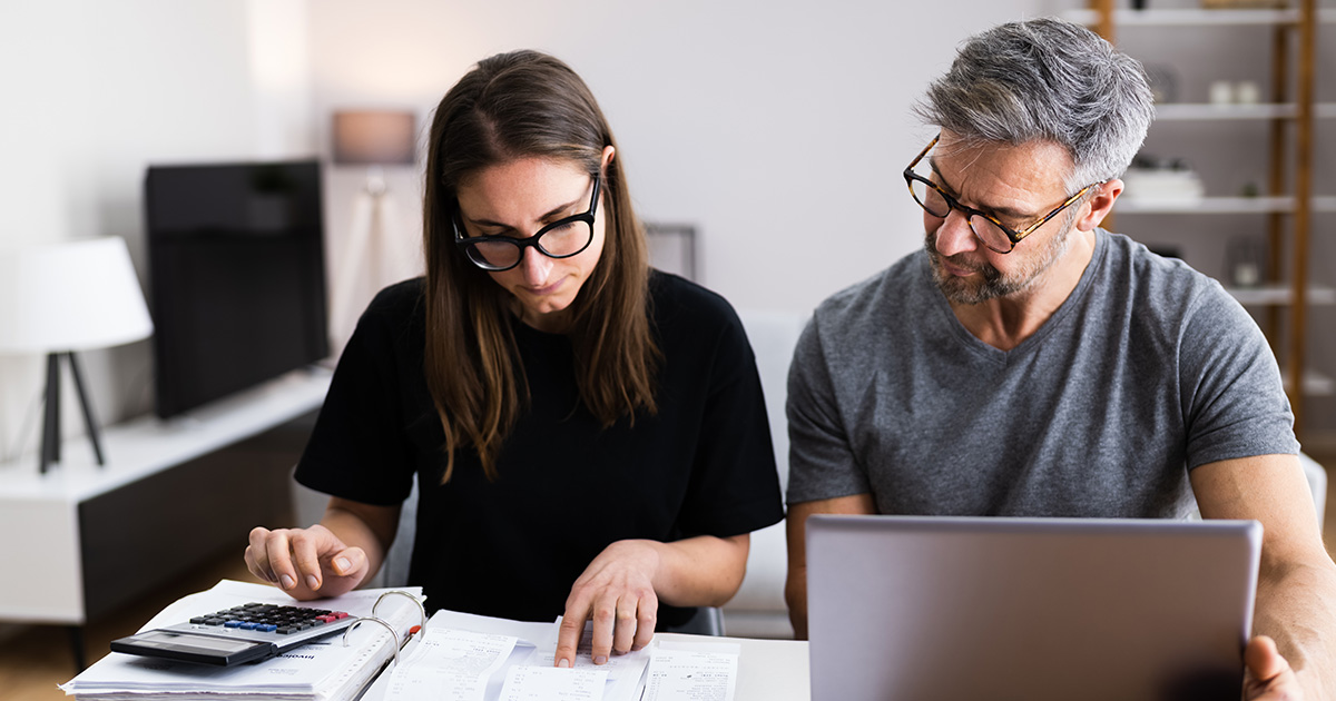 Couple sitting at desk with calculator and laptop reviewing documents 