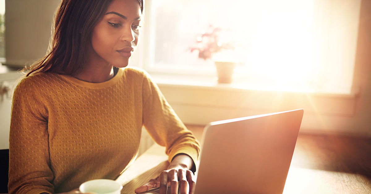 Woman sitting at table holding coffee cup and typing on laptop