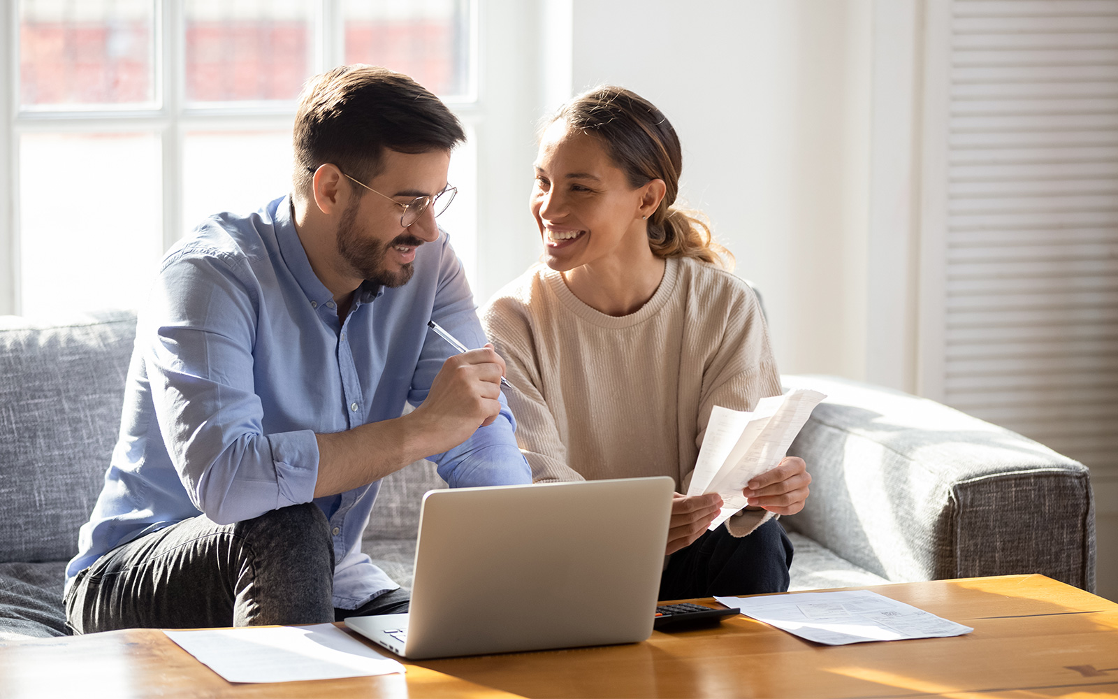 Happy young married couple sit on couch calculate expenses