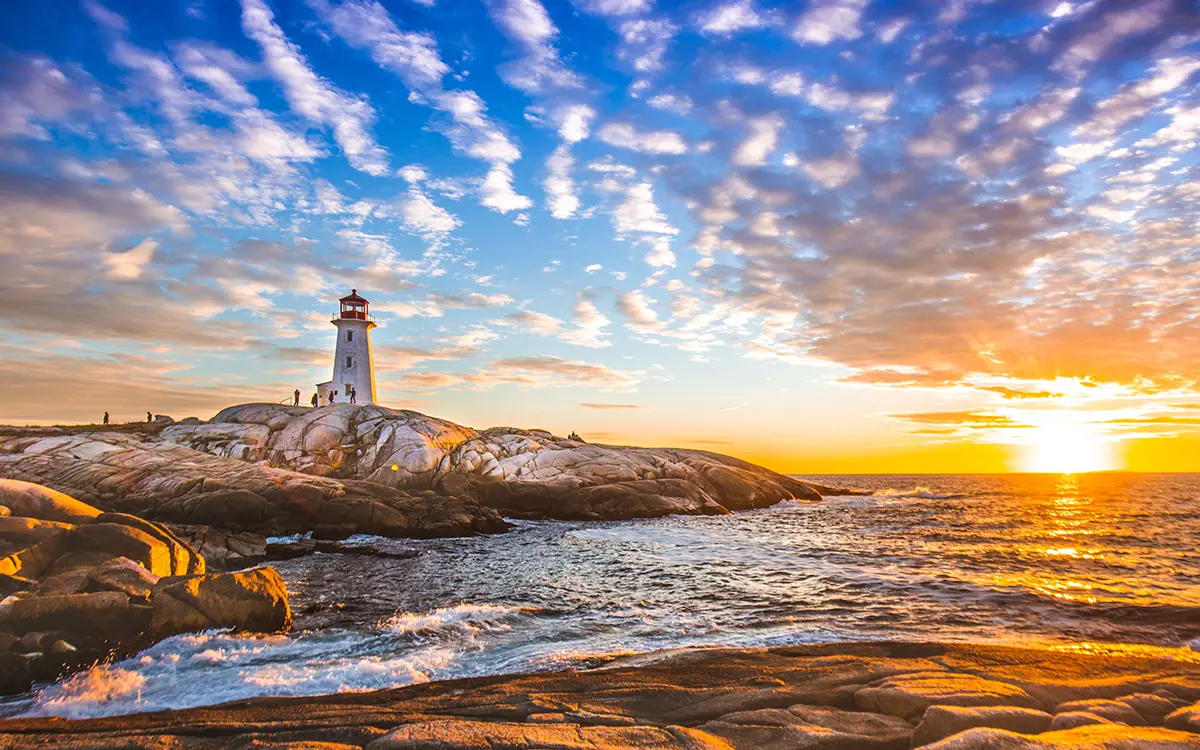 Scenic shot of a sunset over the ocean on to rock land with a light house and people 