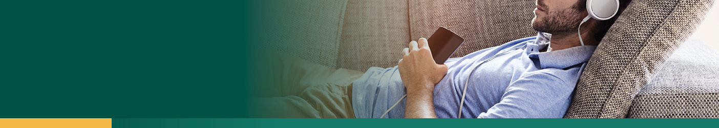 man laying on couch listening to a podcast through headphones